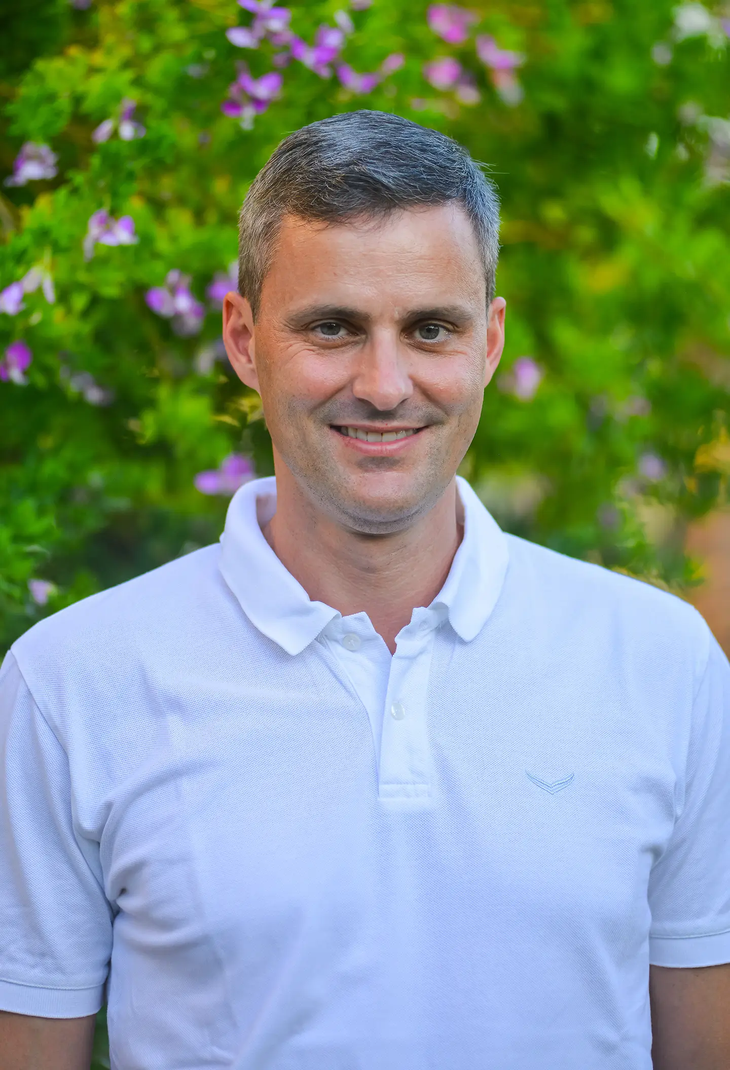 Johannes Köck, freundliches Portrait im weißen Polo vor blühendem Grün